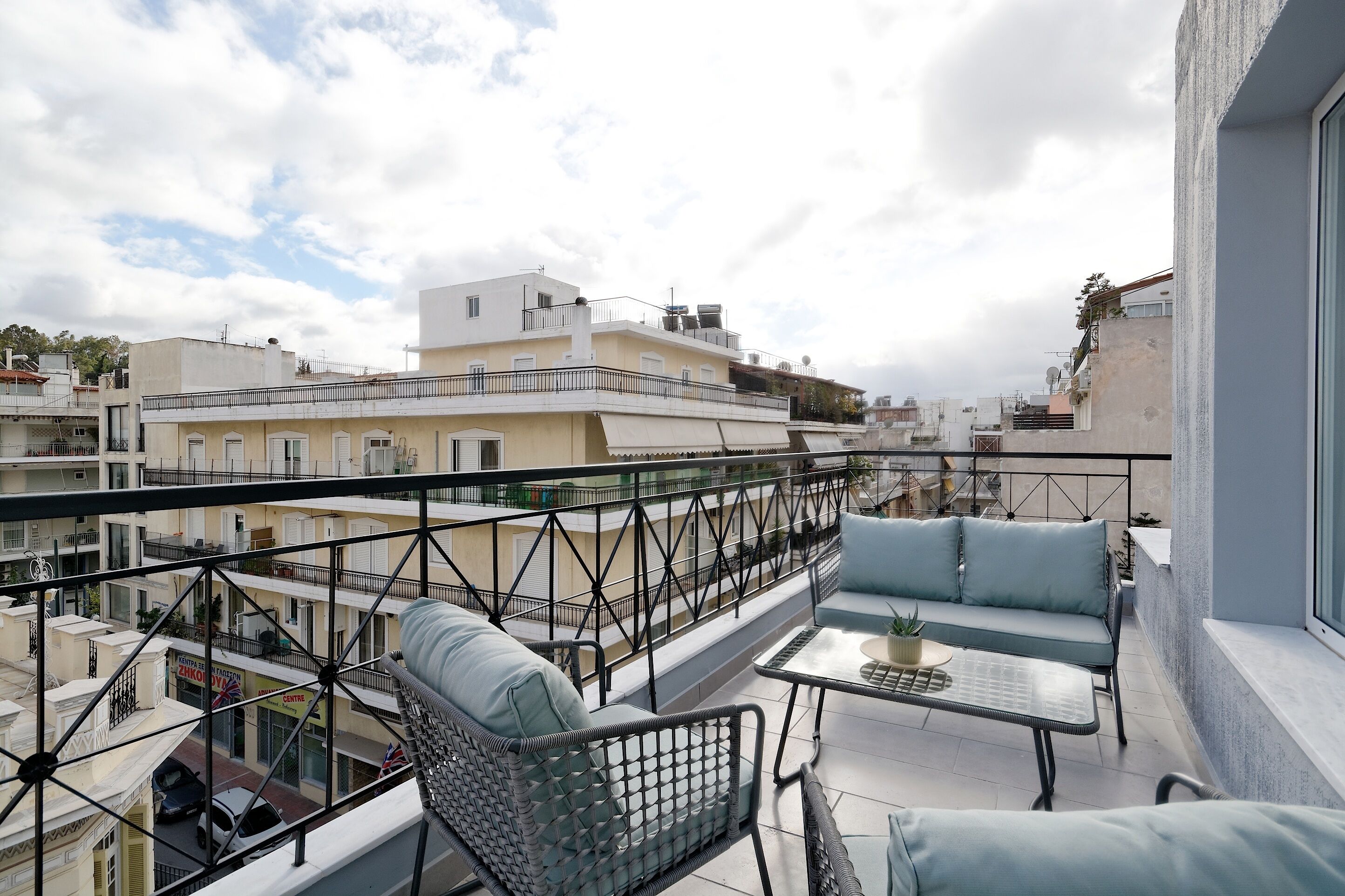 Een balkon met buitenmeubilair en uitzicht op omliggende gebouwen, onder een heldere lucht.