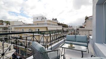 Een balkon met buitenmeubilair en uitzicht op omliggende gebouwen, onder een heldere lucht.
