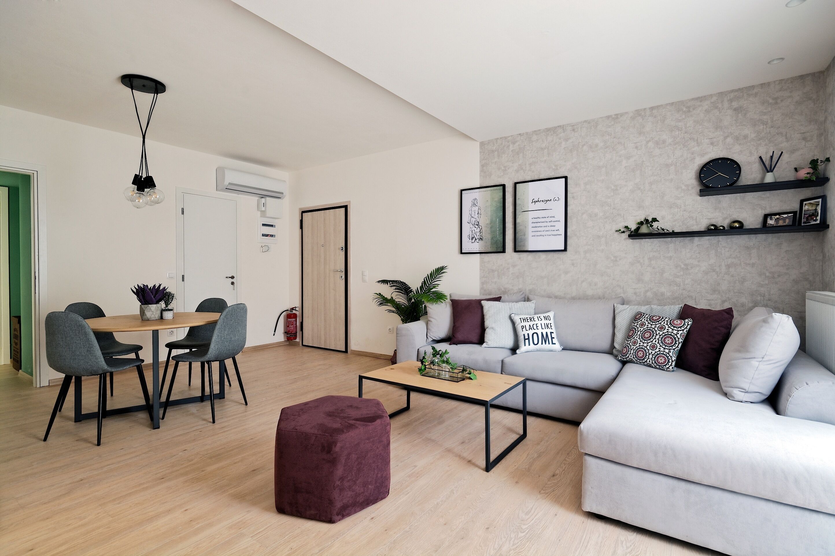 Ein modernes Wohnzimmer mit einem grauen Sofa, einem Holztisch und einem violetten Pouf.