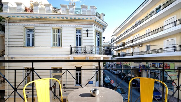 Un balcón con sillas amarillas y una mesa, con vistas a una calle con coches y edificios.