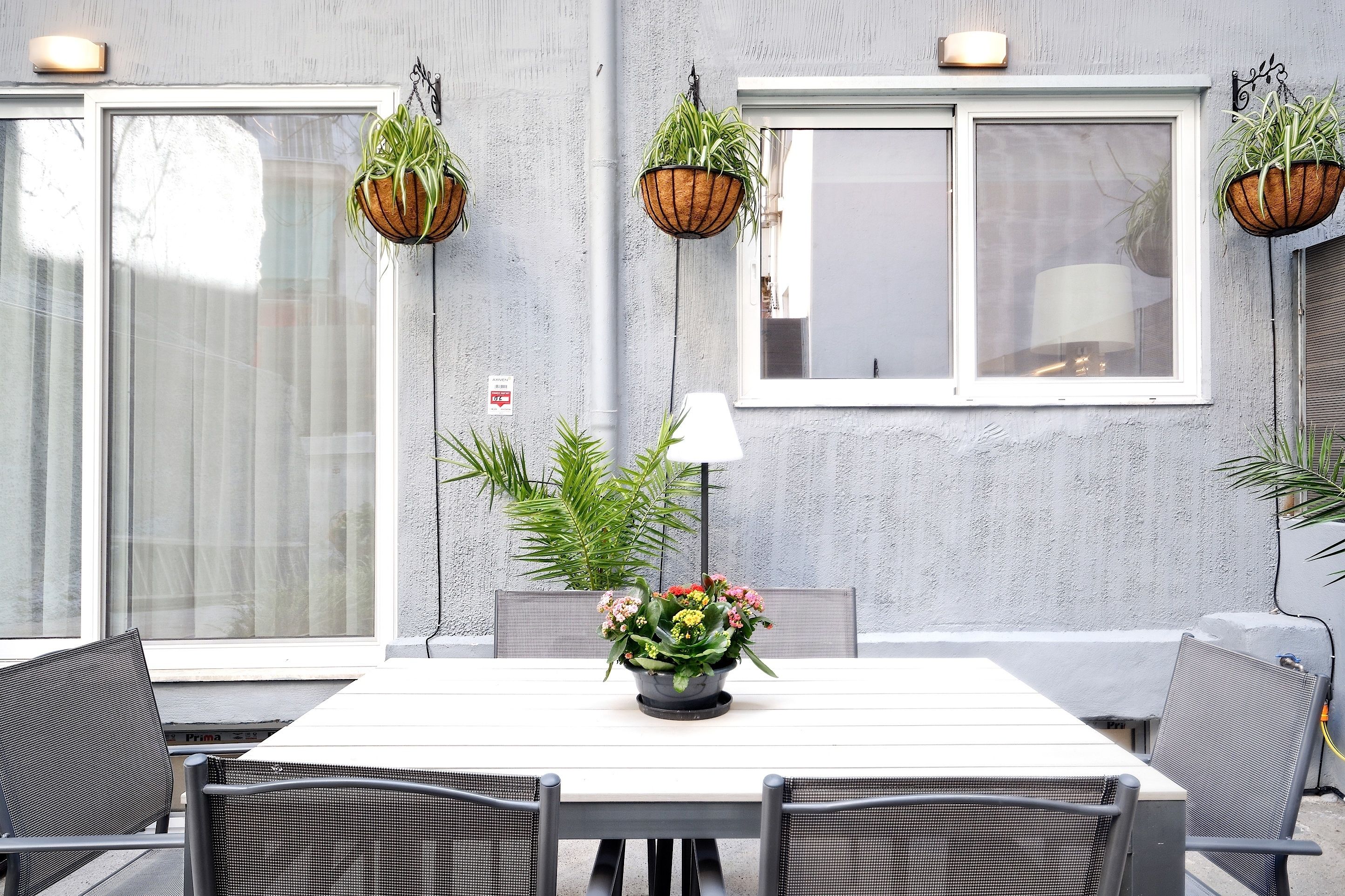 Un comedor con una mesa blanca, sillas negras y macetas colgantes con plantas verdes.