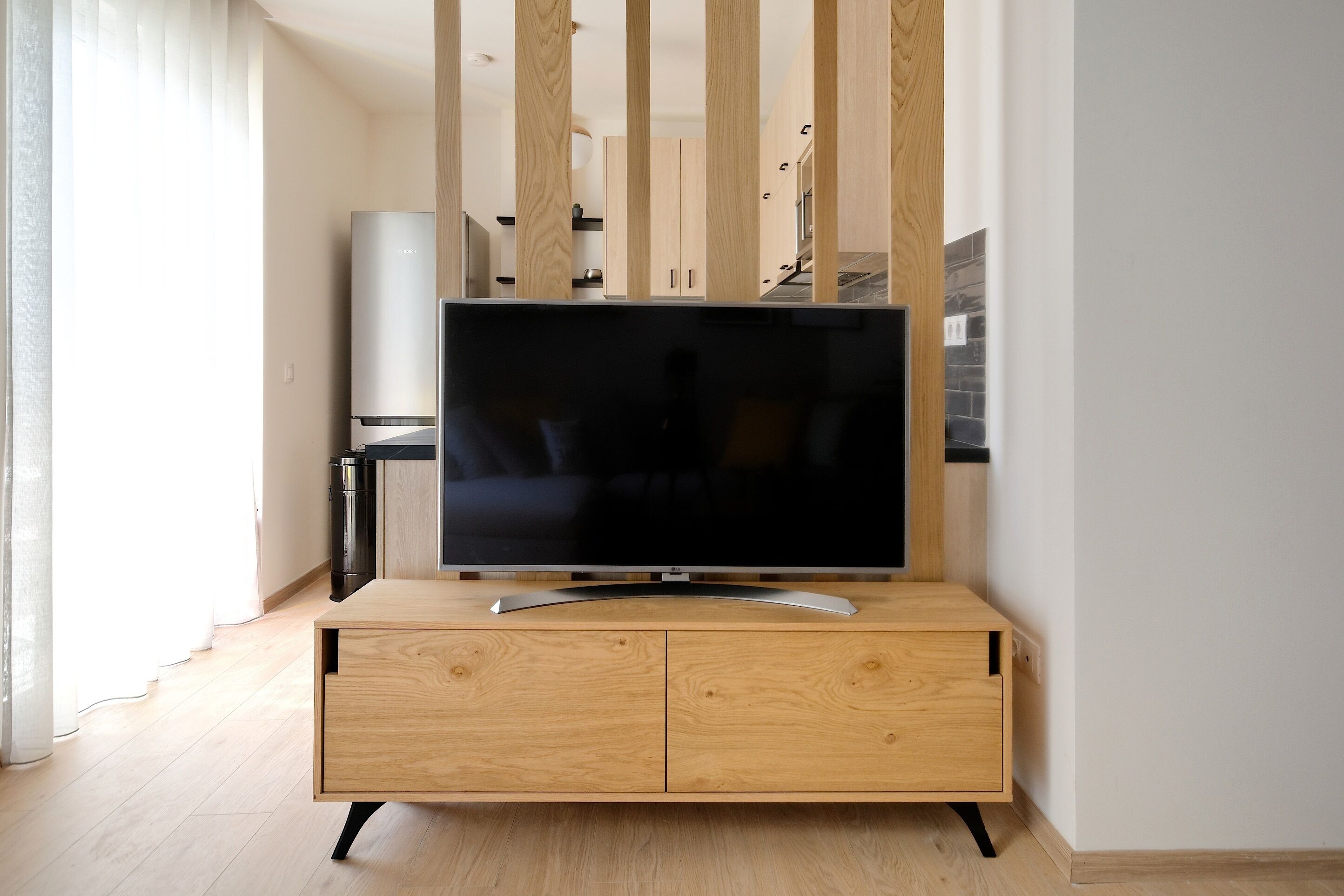 Una cocina moderna con una TV integrada en un mueble de madera, un refrigerador y un microondas.