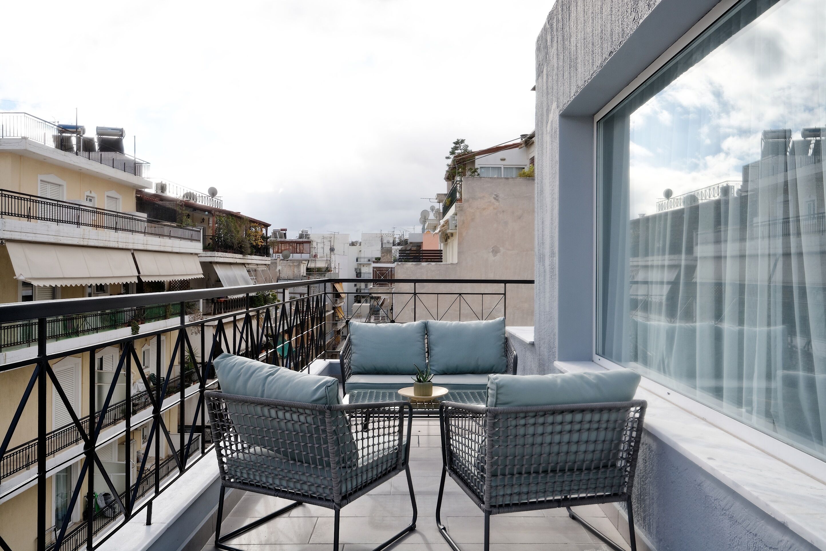 A rooftop terrace with wicker furniture, a small table, and a view of the cityscape.