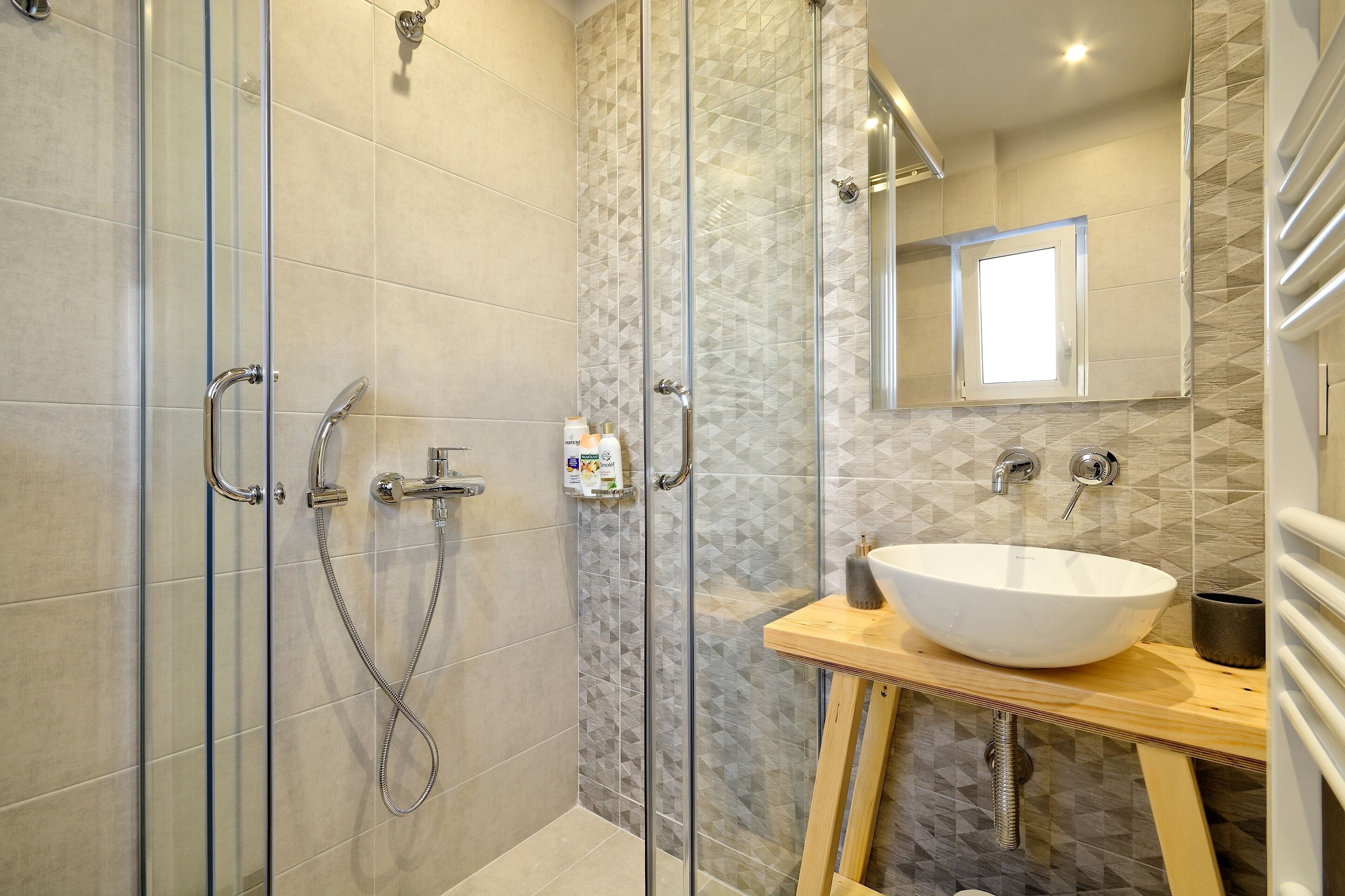 A modern bathroom with a glass-enclosed shower, a wooden vanity with a white sink, and a large mirror above the sink.