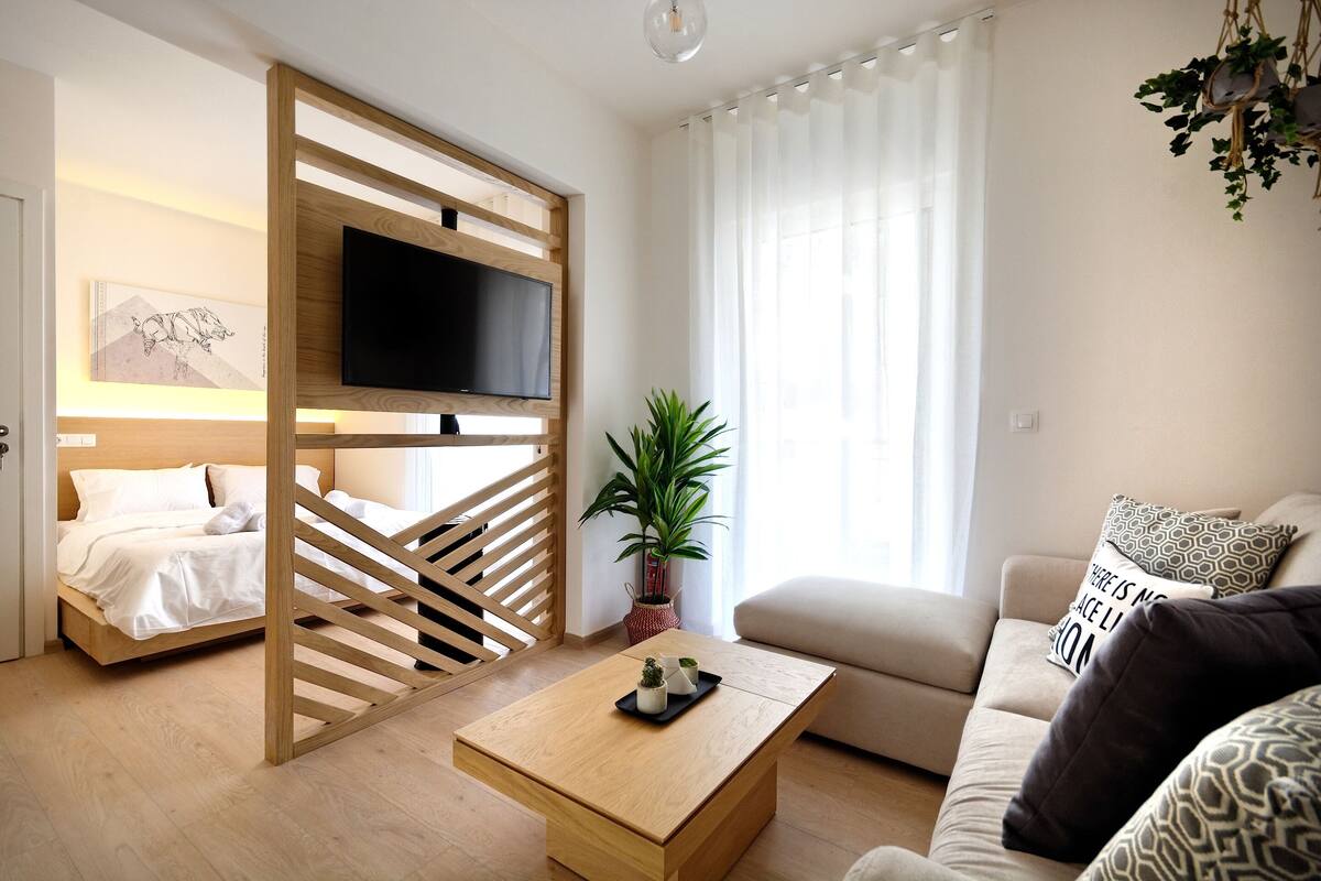 Una sala de estar moderna con una cama, un sofá, una mesa de centro y un televisor montado en un panel de madera.