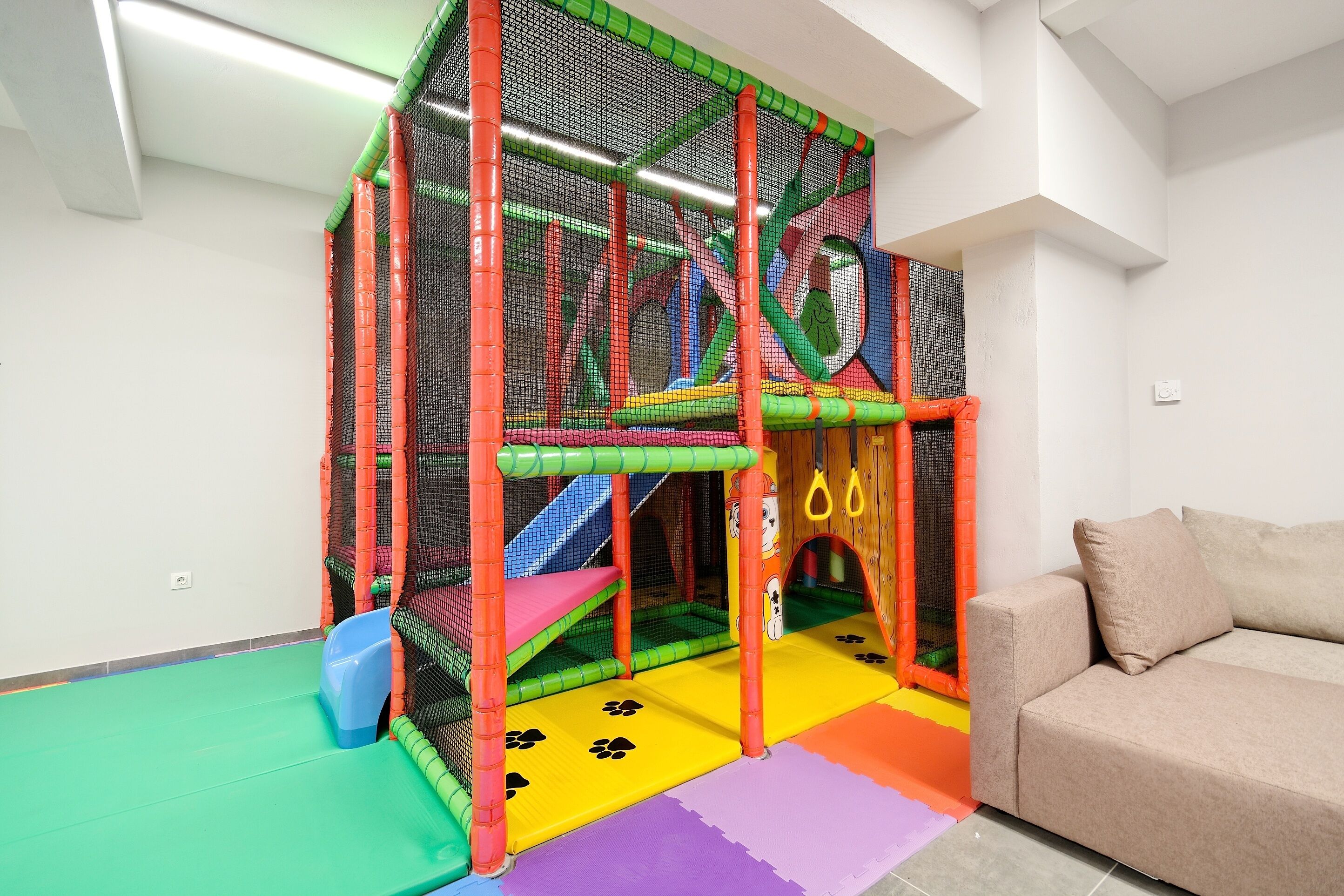 A play area with a netted enclosure, a slide, and a soft play floor.