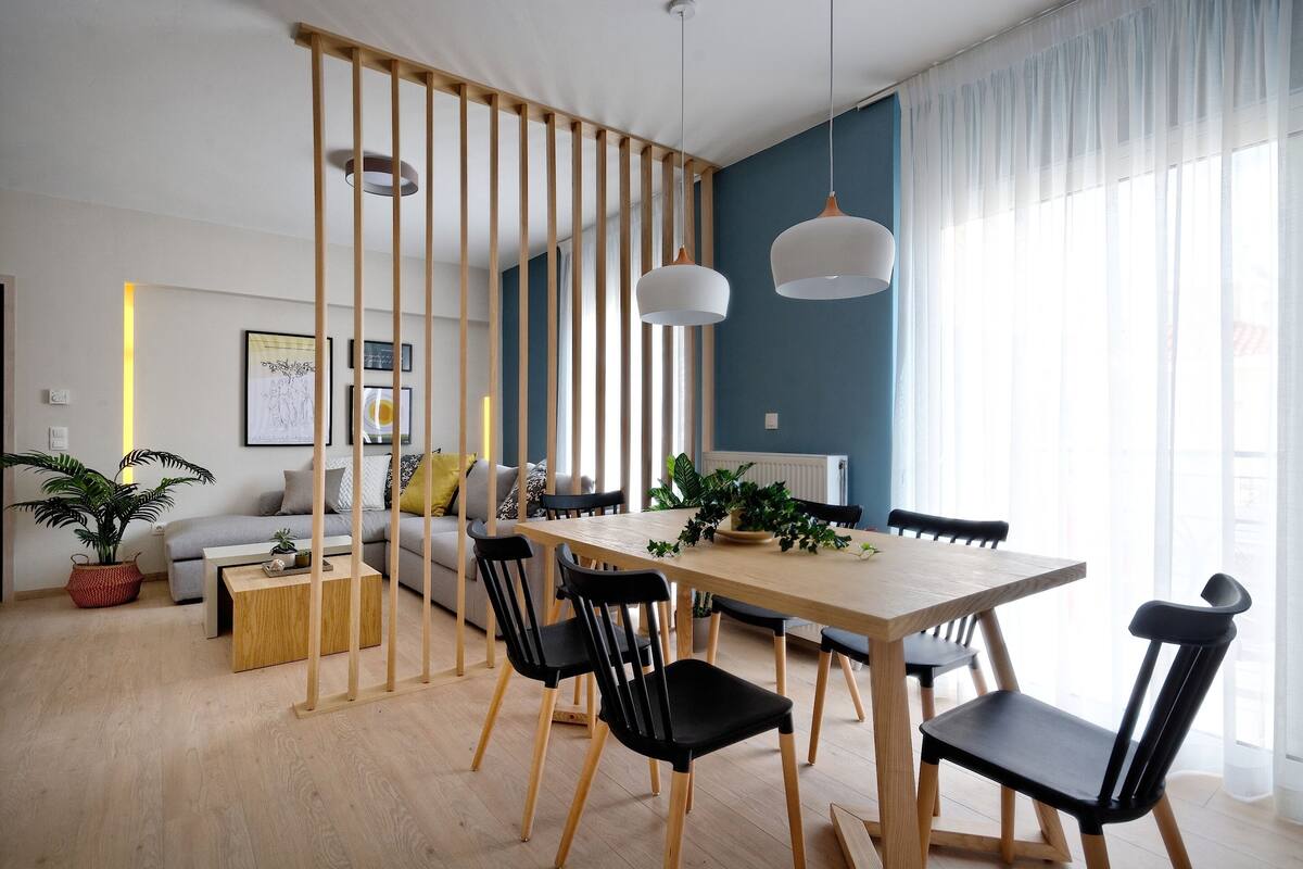 Una sala de estar moderna con comedor, que incluye una mesa de comedor de madera, sillas negras, un sofá y un ventanal con cortinas translúcidas.