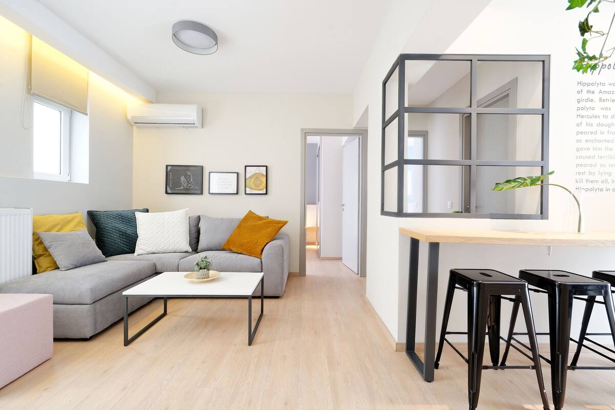 Una sala moderna con un sofá gris, una mesa de centro blanca y taburetes negros.