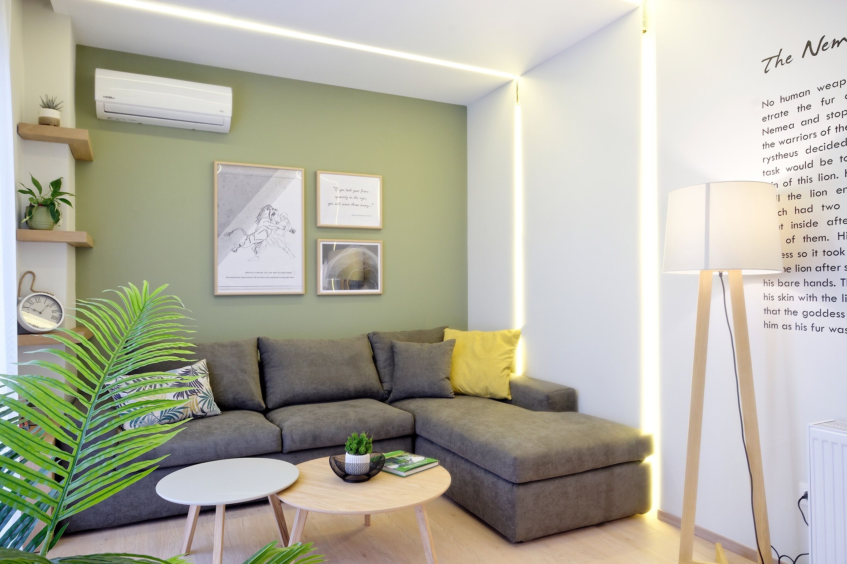 A modern living room with a grey sectional sofa, a round coffee table, and a floor lamp. There are wall-mounted shelves with plants and framed artwork.