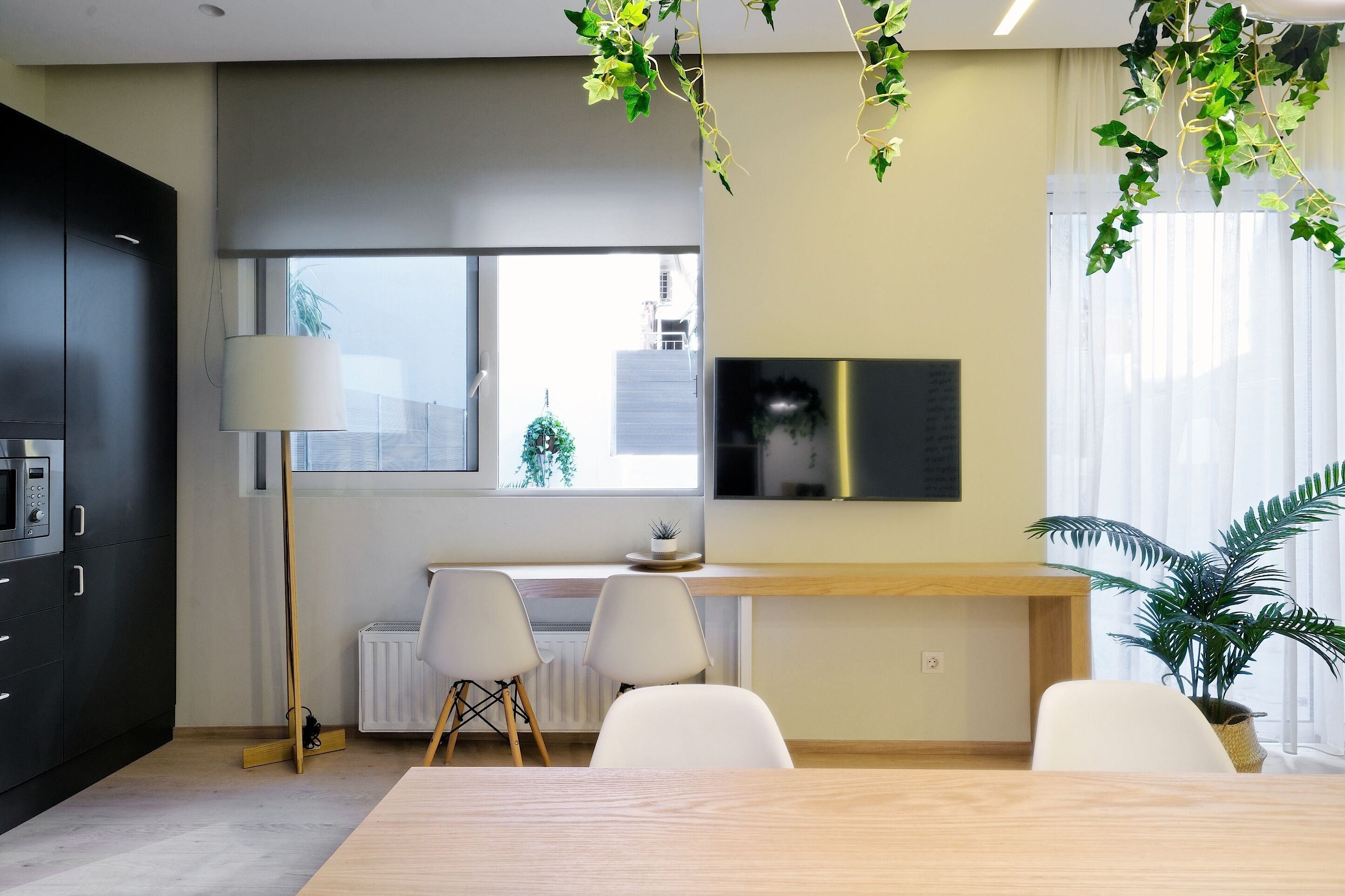Een moderne keuken met een eethoek, voorzien van een groot raam, een inbouwmagnetron en een houten eettafel met stoelen.