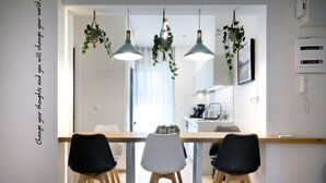 Un comedor moderno con una mesa de madera, sillas blancas y negras, plantas colgantes e iluminación colgante.