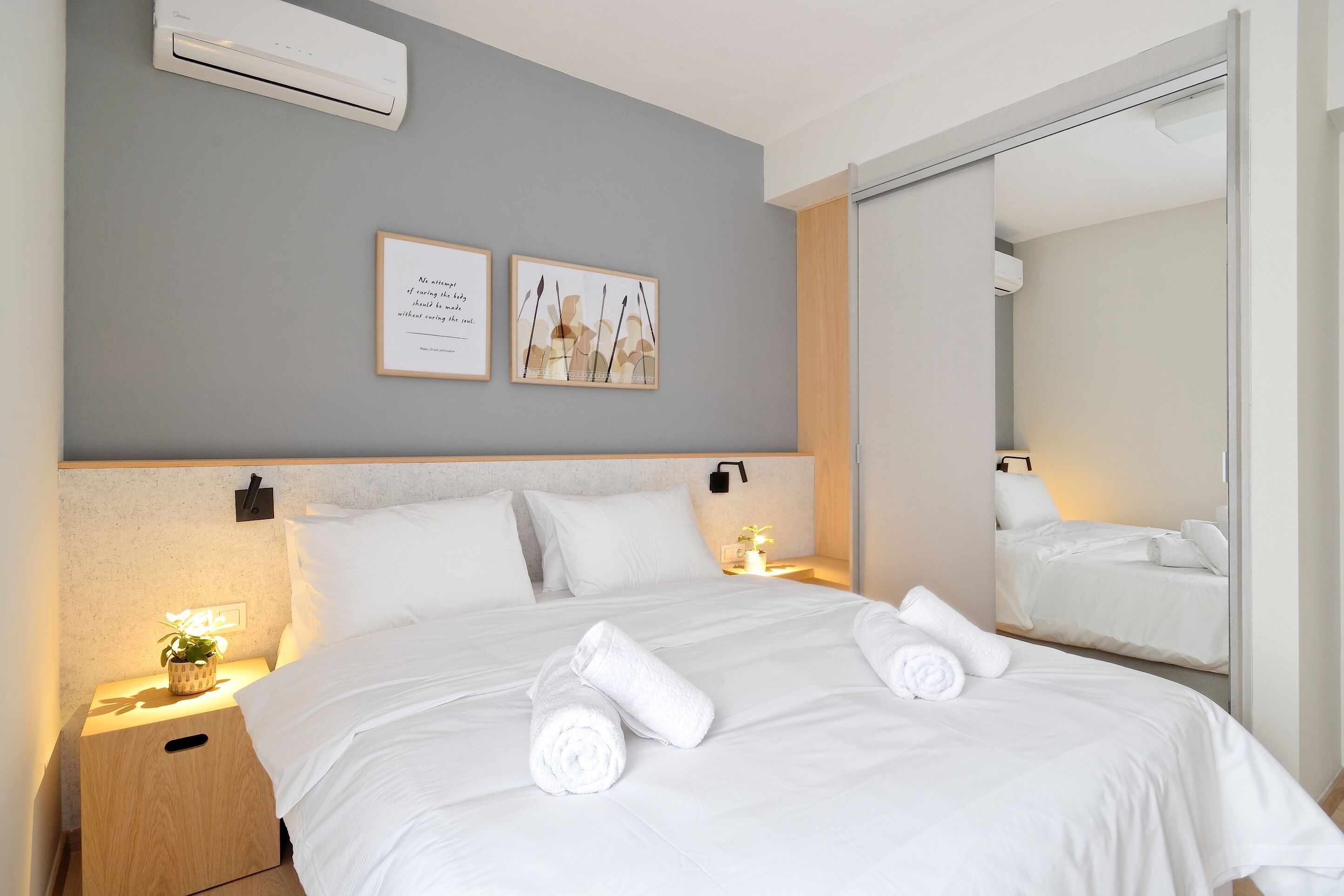 A neatly made bed with white linens and towels, a bedside lamp, and a framed quote on the wall.