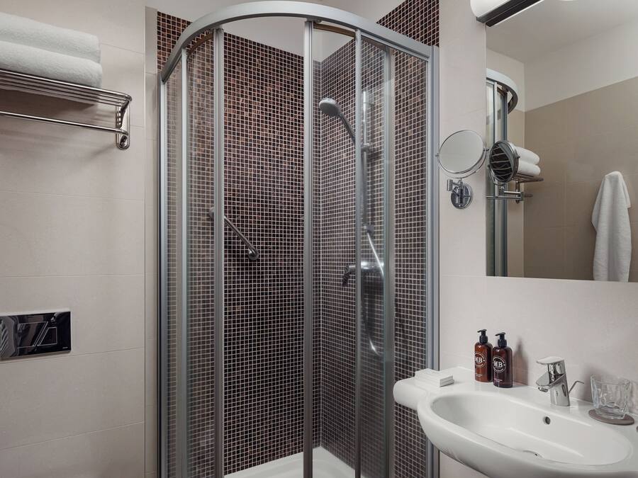 Un baño moderno con ducha de vidrio, lavamanos con espejo y artículos de aseo en la encimera.