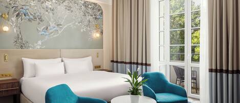 A hotel room with a large bed, two armchairs, a small table with a plant, and a wall with a floral mural.