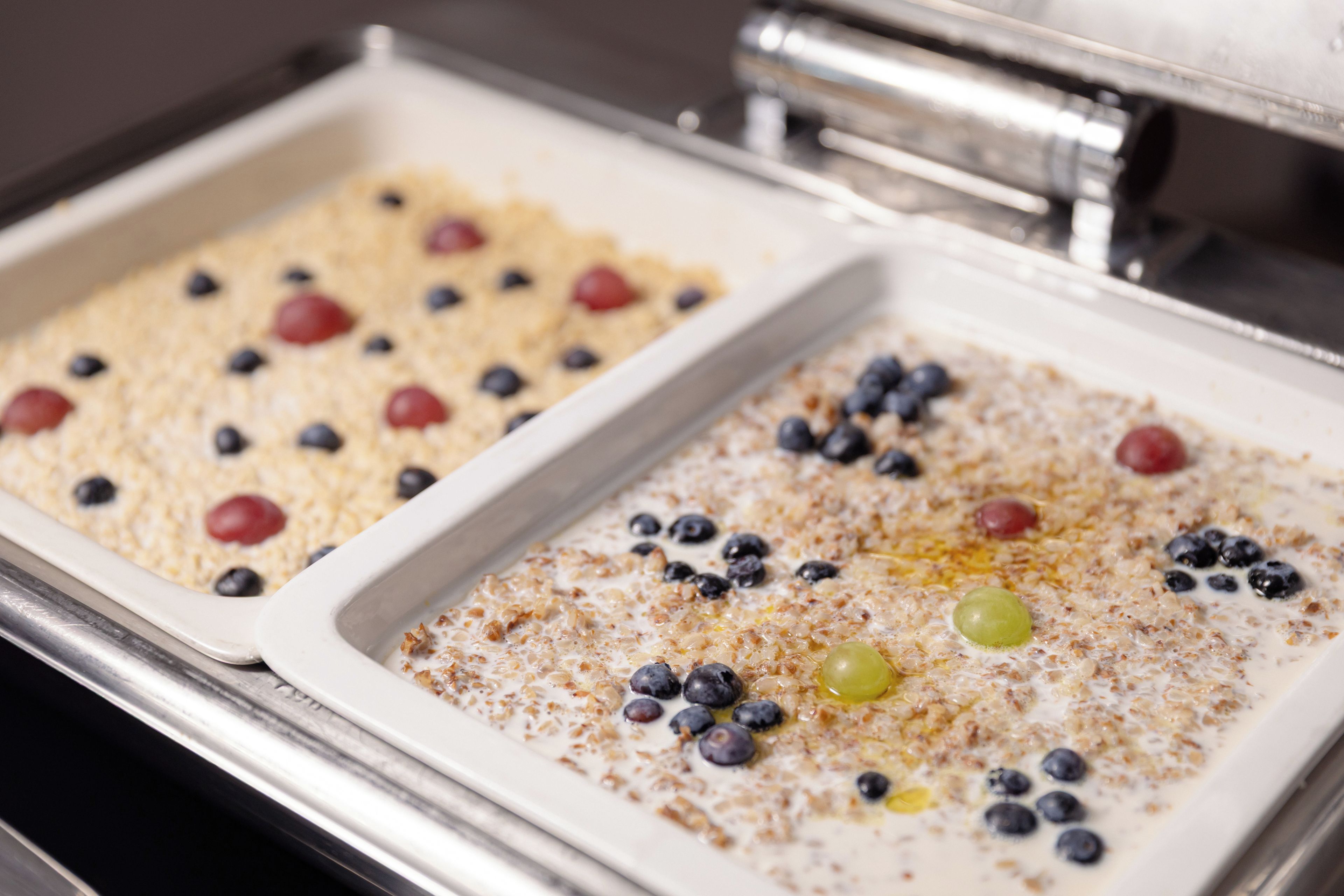 Two white rectangular trays with food items, possibly oatmeal or porridge, topped with blueberries and a few other berries.
