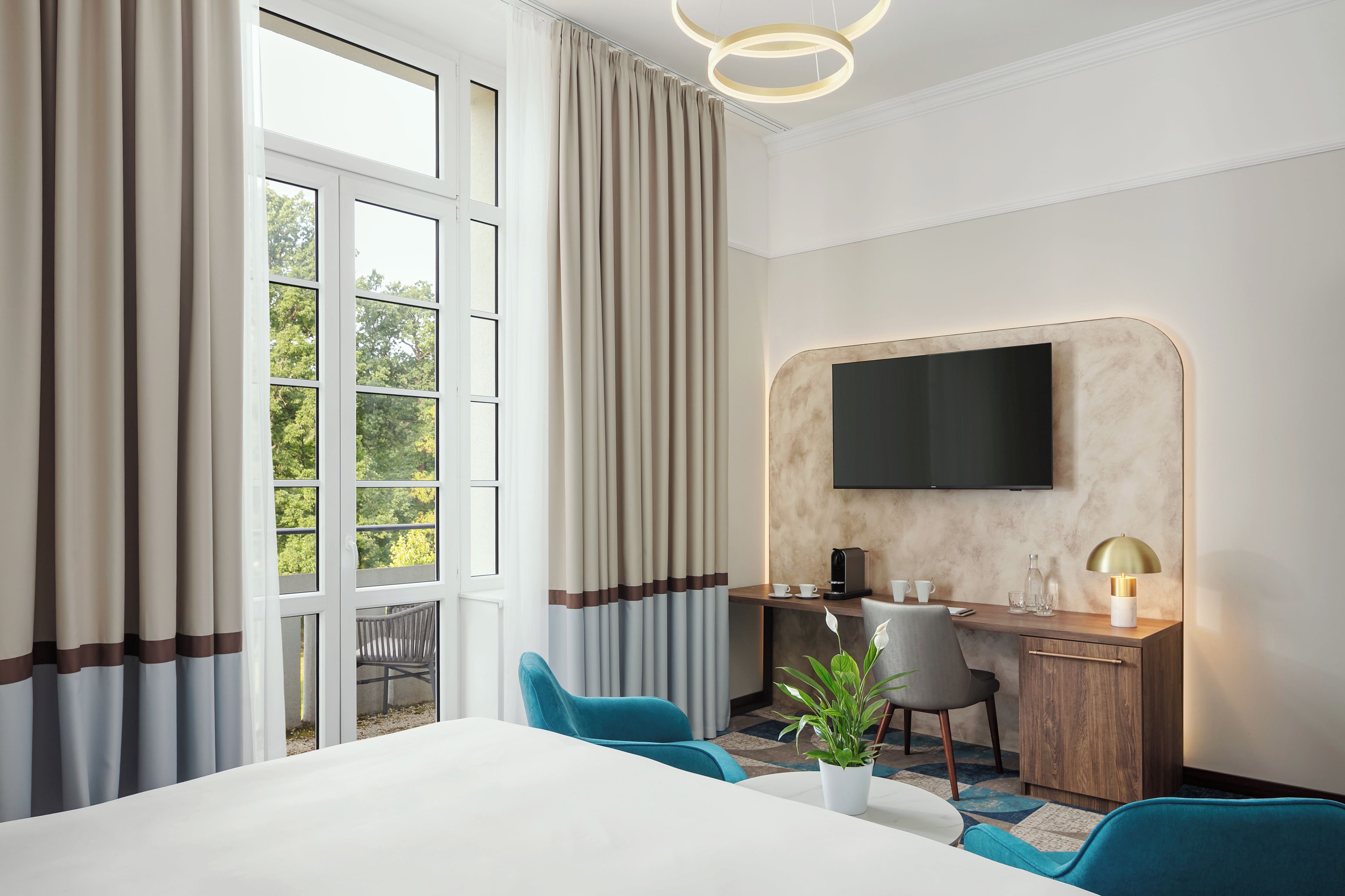 Habitación de hotel con una cama grande, un escritorio con silla, televisor montado en la pared y ventana con cortinas.