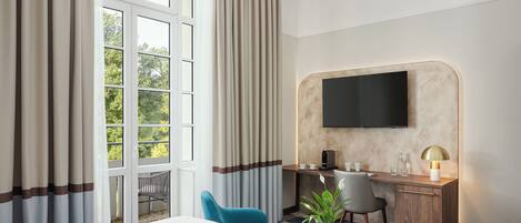 Habitación de hotel con una cama grande, un escritorio con silla, televisor montado en la pared y ventana con cortinas.