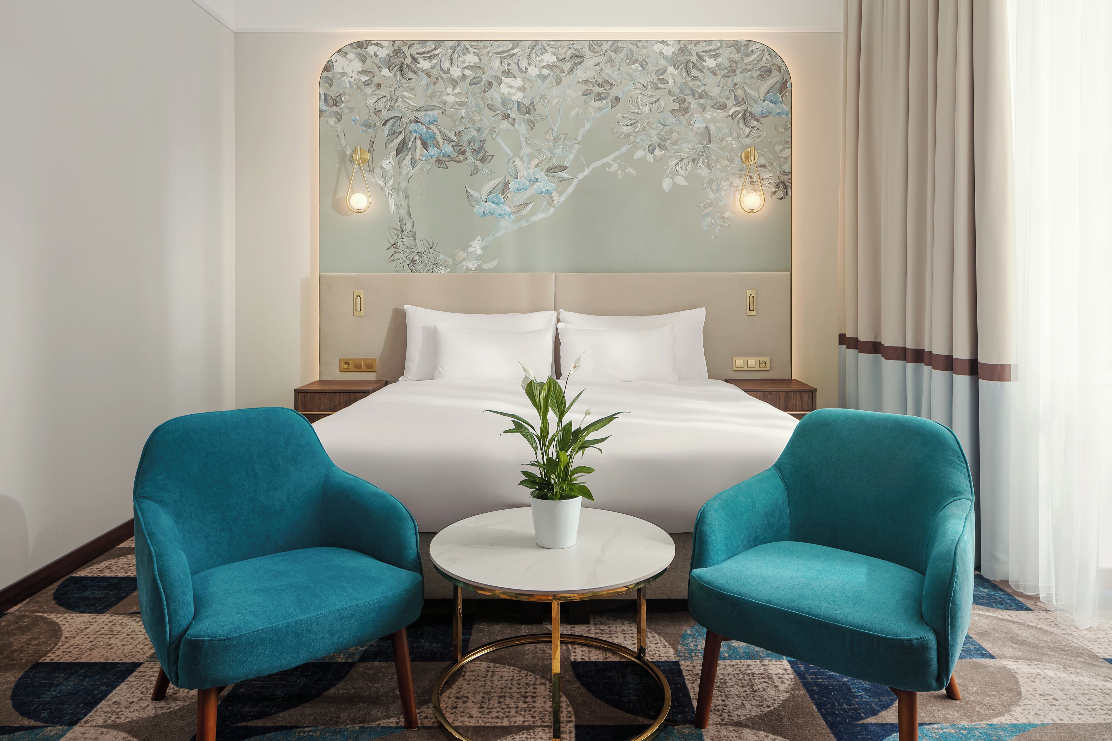 A hotel room with a bed, two chairs, a small table, and a decorative wall.