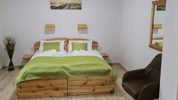 Quarto com cama de madeira, roupa de cama verde, uma pequena escrivaninha, uma cadeira, um espelho e um quadro na parede.