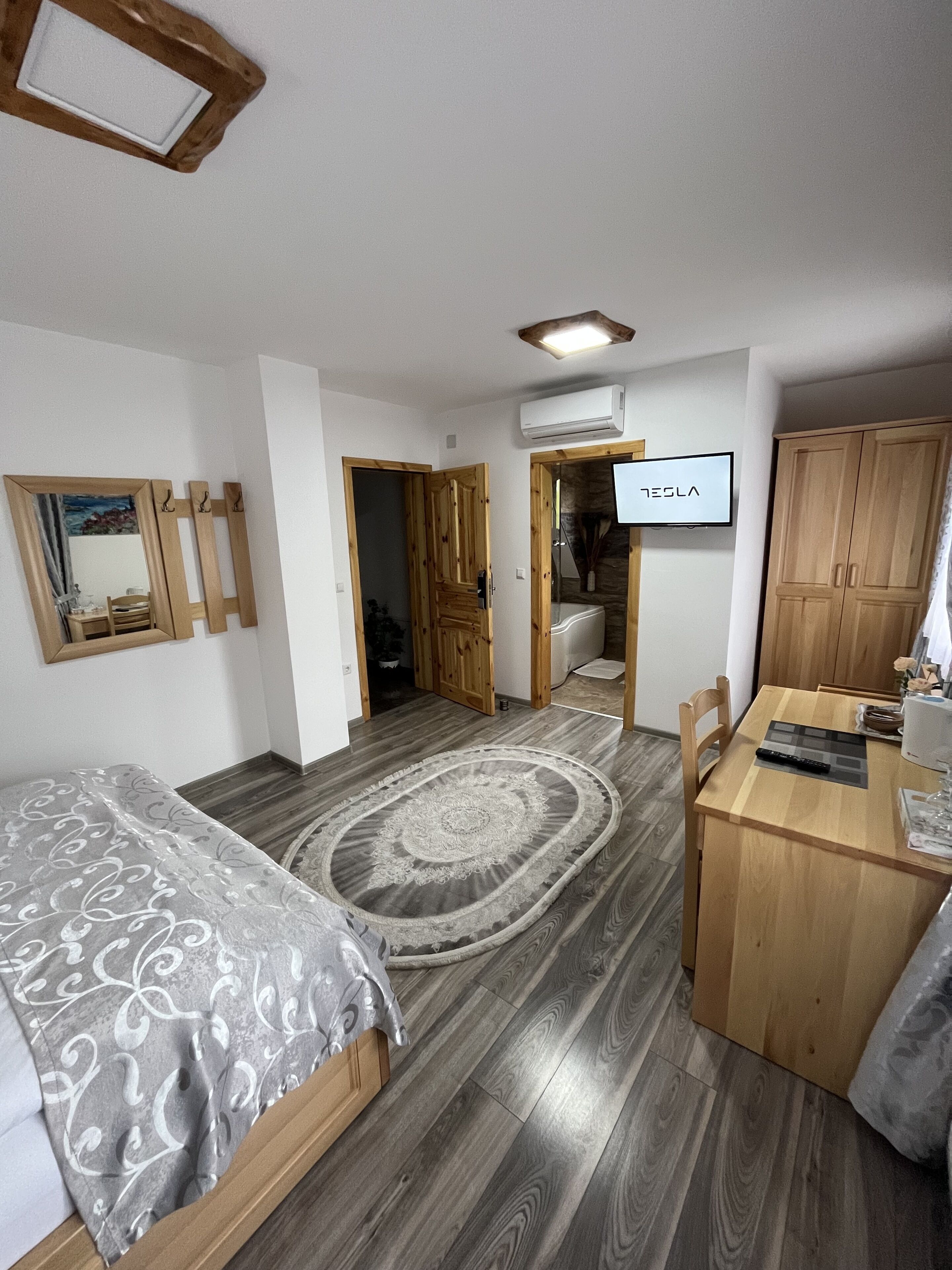 Quarto compacto com cama, escrivaninha de madeira, televisão e armário.