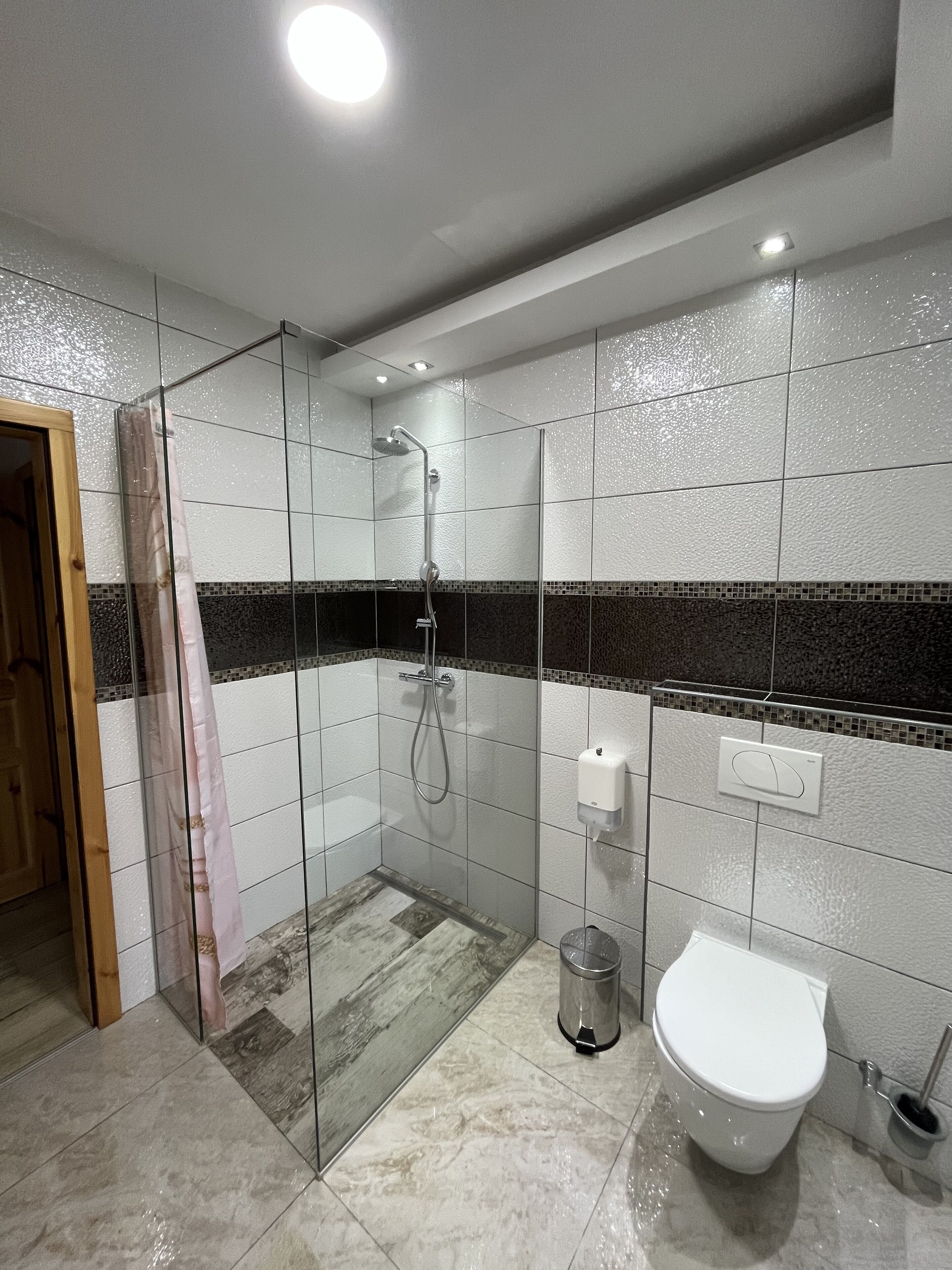 A modern bathroom with a glass shower enclosure, a toilet, and a hand dryer.