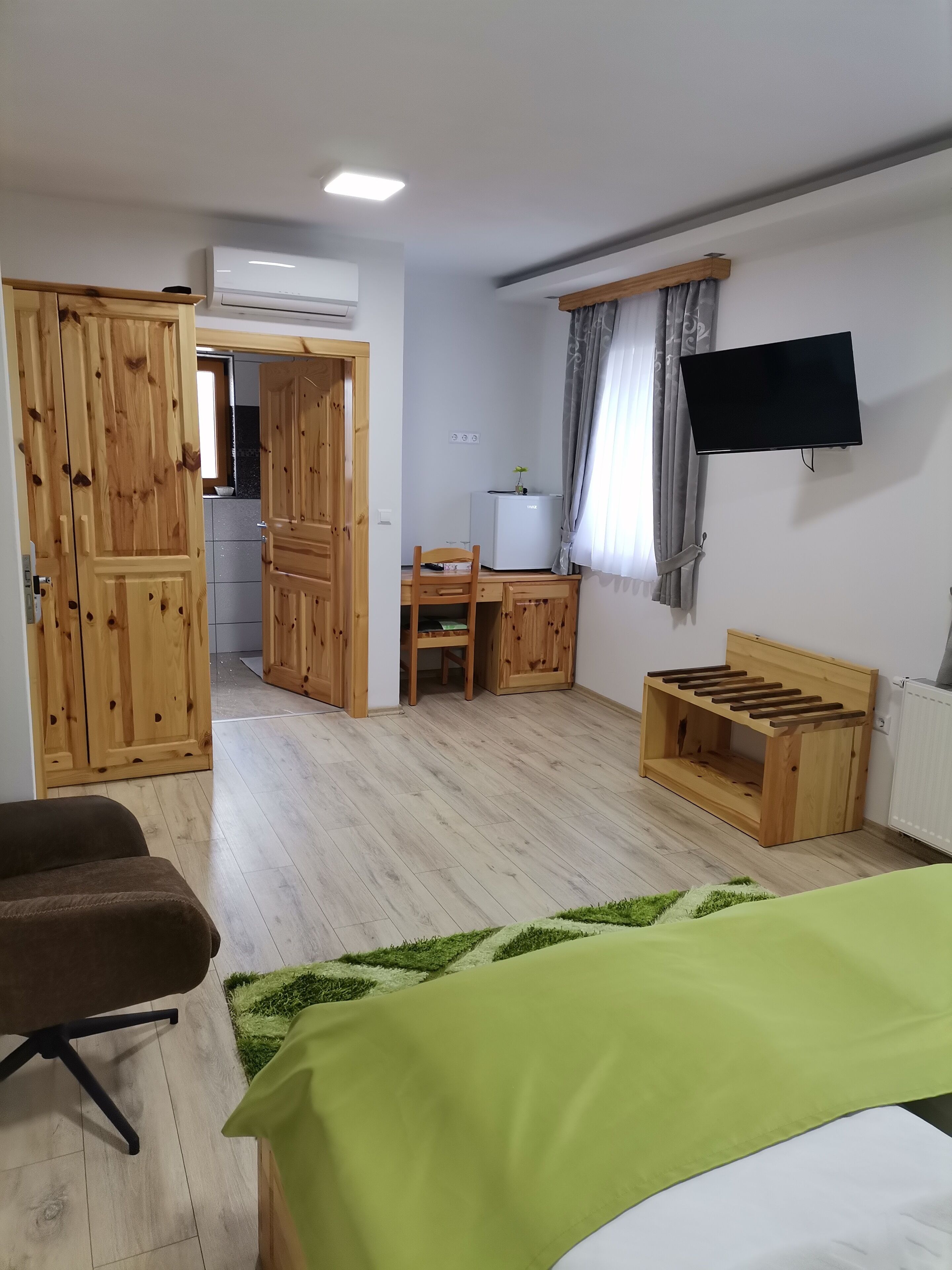 Quarto com cama, escrivaninha, cadeira, televisão e guarda-roupa de madeira.