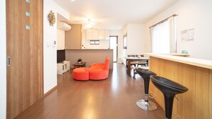 A modern kitchen with wooden cabinets, a dining area with a table and chairs, and a bright ceiling light. - Kyoto Guesthouse Kyozui (Kyoto)