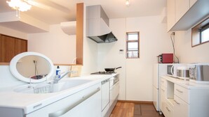 A modern kitchen with white cabinetry, a stove, a microwave, and a sink with a mirror. - Kyoto Guesthouse Kyozui (Kyoto)