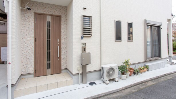 A modern building with a white facade, a wooden door, and a small air conditioning unit on the sidewalk. - Kyoto Guesthouse Kyozui (Kyoto)