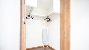 A room with a wooden floor, a white wall, and a wooden door. There is a clothes drying rack with hangers and a white ironing board. - Kyoto Guesthouse Kyozui (Kyoto)