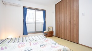 A bedroom with a bed, a wooden wardrobe, a window with blue curtains, and a small table with a chair. - Kyoto Guesthouse Kyozui (Kyoto)