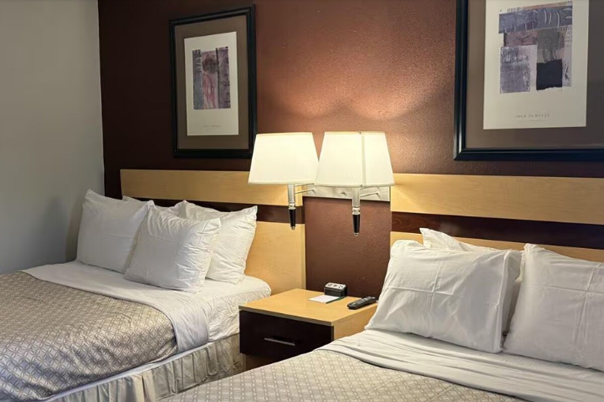 A hotel room with two beds, a nightstand with a lamp, and framed artwork on the wall.
