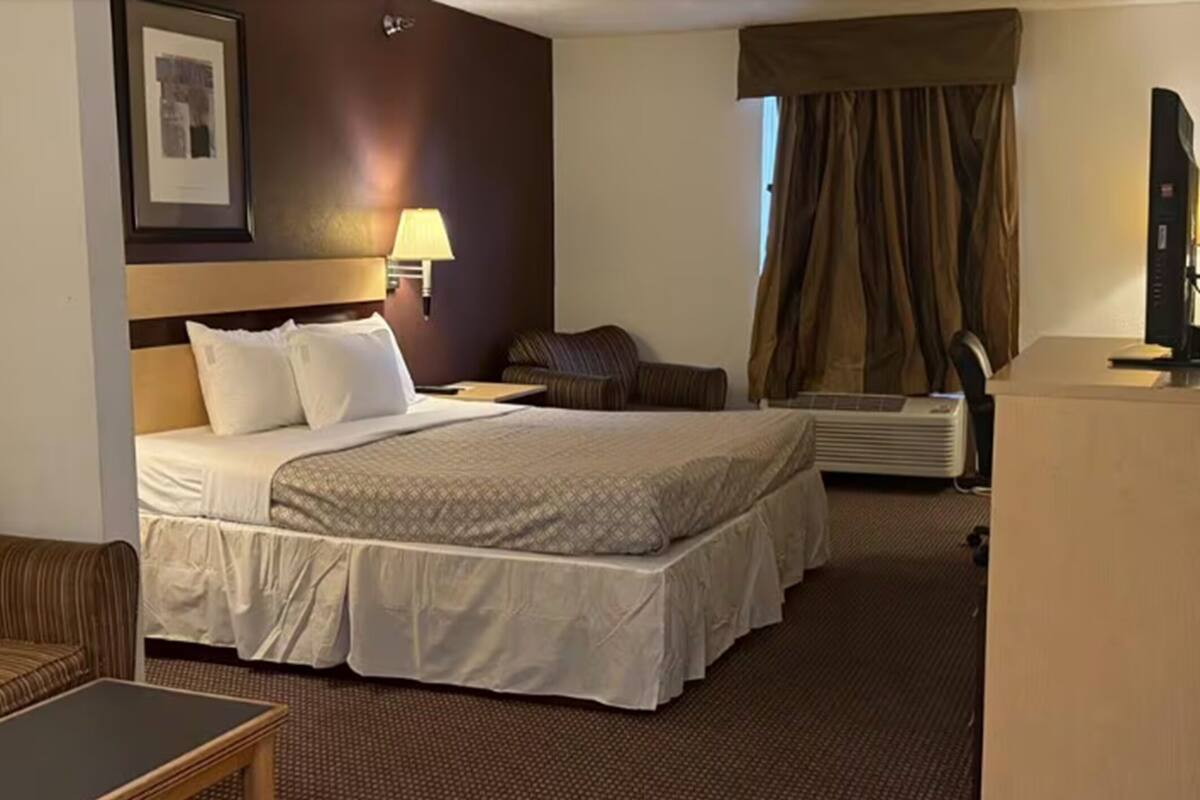A hotel room with a large bed, a desk, a chair, a lamp, a television, and a window with curtains.