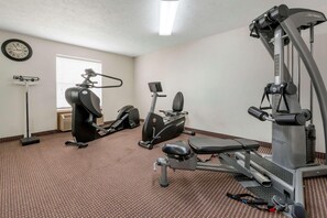 Ein Fitnessraum mit Cardiogeräten, einer Hantelbank und einer Wanduhr.