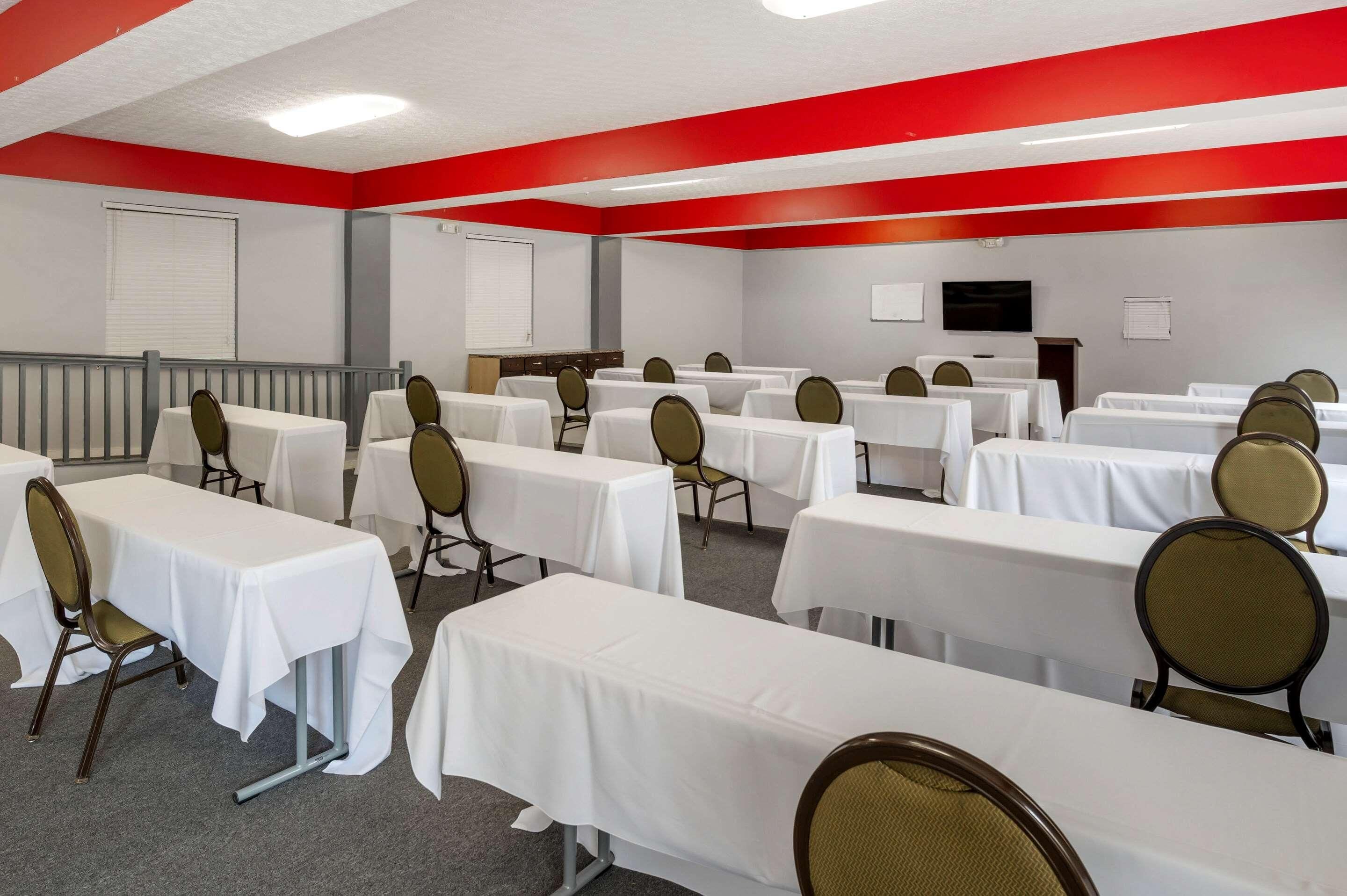 A conference room with multiple tables and chairs, a whiteboard, and a television on the wall.