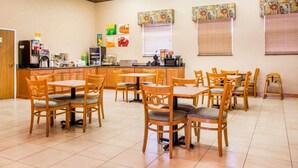 A dining area with multiple tables and chairs, a kitchen counter with appliances, and decorative wall art. - Surestay Best Western Obetz Rickenbacker Airport (Columbus)