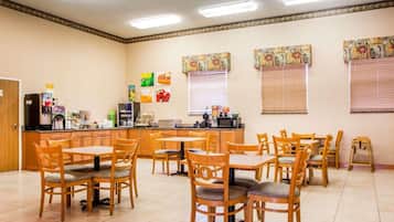 A dining area with multiple tables and chairs, a kitchen counter with appliances, and decorative wall art.
