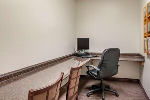 Egy kis iroda, amelyben van egy íróasztal, két szék, egy számítógép és egy televízió.