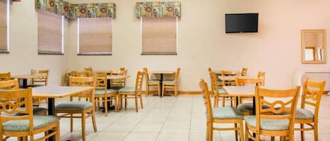 Un comedor con mesas y sillas de madera, un televisor de pantalla plana en la pared y cortinas con diseños.