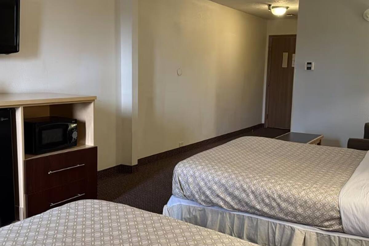 A hotel room with two beds, a desk with a microwave, and a door leading to another room.