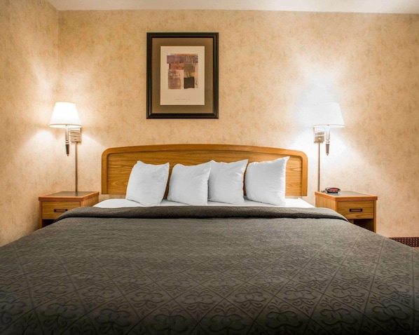 Ein Hotelzimmer mit einem großen Bett, zwei Nachttischen, einem gerahmten Bild an der Wand und zwei Wandleuchten.