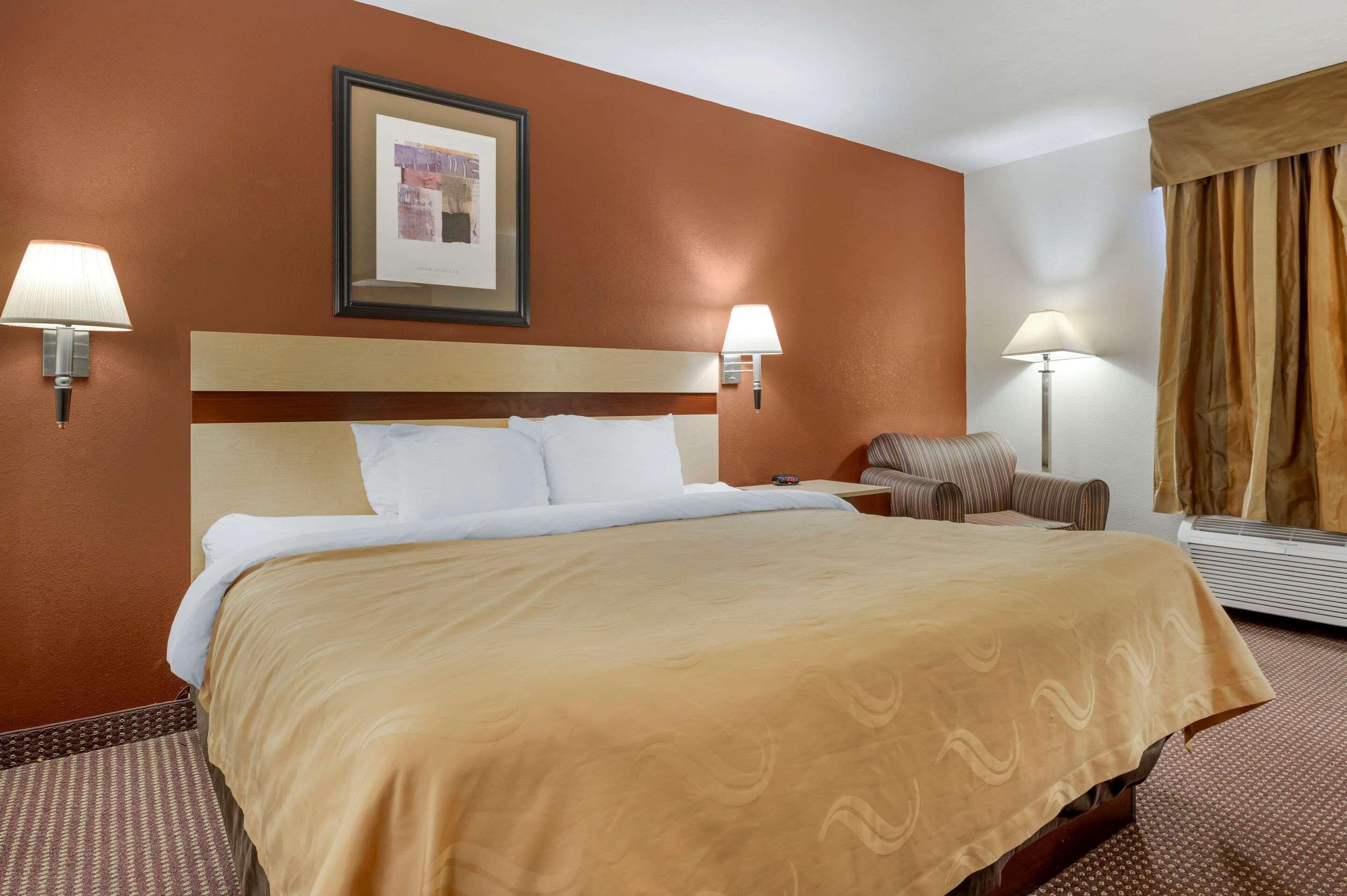 Camera d'albergo con un letto grande, due abat-jour, un quadro appeso al muro e una finestra con tende.