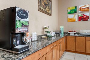 A coffee machine with options for coffee, hot water, and decaf, a bowl of fruit, and a waffle plate on a granite countertop in a kitchen. - Surestay Best Western Obetz Rickenbacker Airport (Columbus)