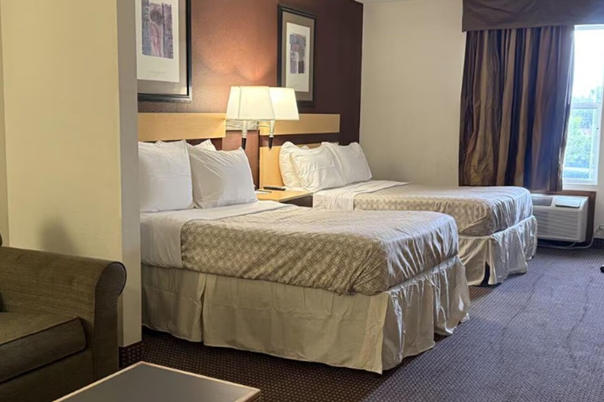 A hotel room with two beds, a desk, a chair, and a window with curtains.