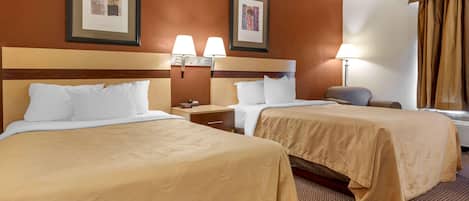 A hotel room with two beds, a nightstand, a lamp, and framed pictures on the wall.