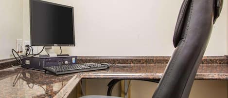 A hotel workspace with a desktop computer, keyboard, and a leather chair.