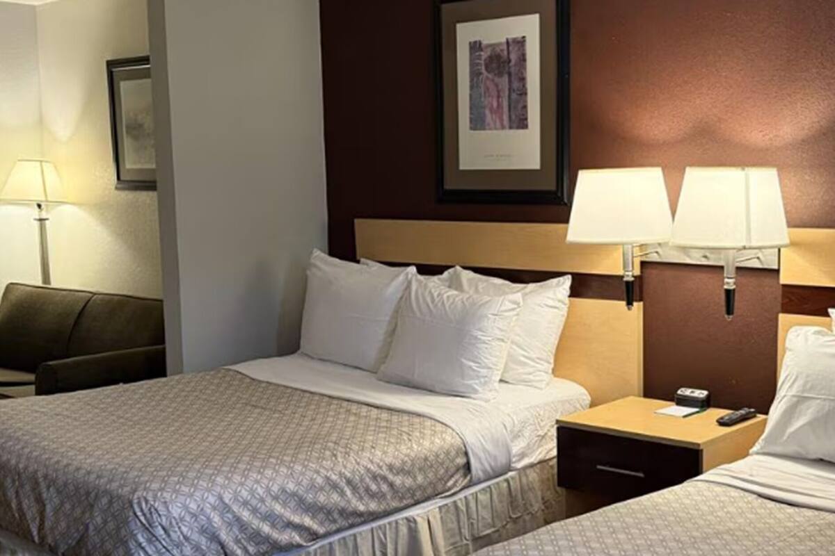 A hotel room with a bed, two bedside lamps, a nightstand, a chair, and a framed picture on the wall.