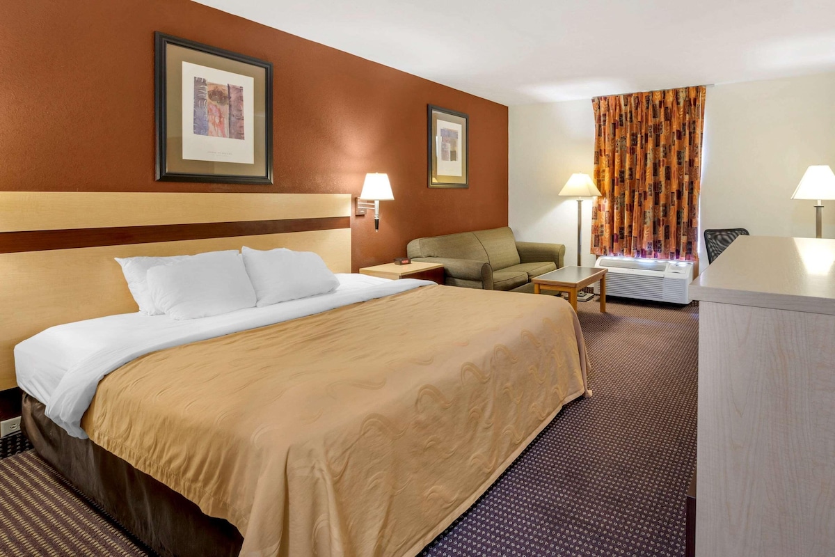 A hotel room with a large bed, a sofa, a desk, and two lamps.