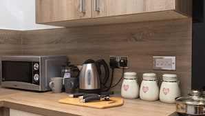Een keuken met een magnetron, waterkoker, koffiezetapparaat en potten op het aanrecht.
