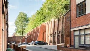 Een smalle straat met geparkeerde auto's, bakstenen gebouwen en bomen.